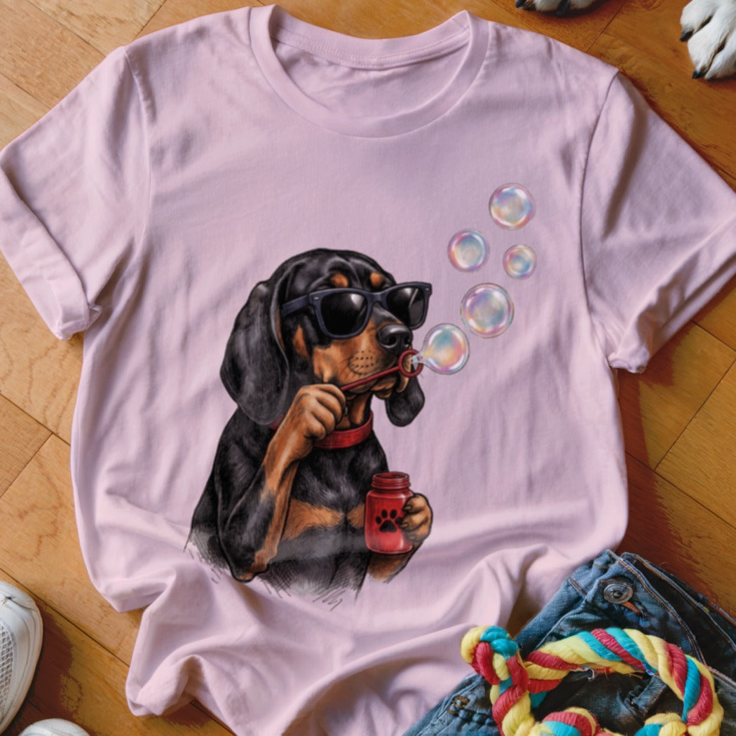 A light pink t-shirt featuring a graphic of a black and tan dog wearing sunglasses and blowing bubbles.