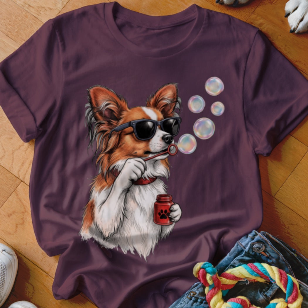 A purple t-shirt featuring a graphic of a long-haired dog wearing sunglasses and blowing bubbles.