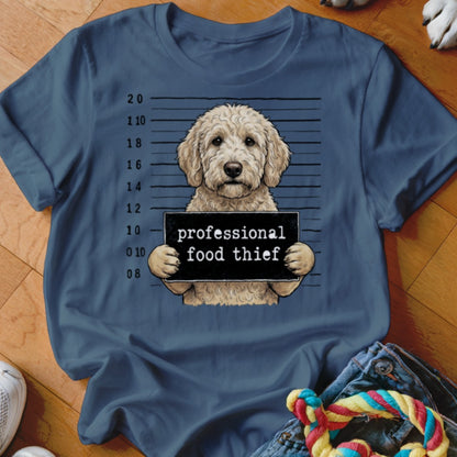 Goldendoodle mugshot with "professional food thief" sign on a navy shirt.
