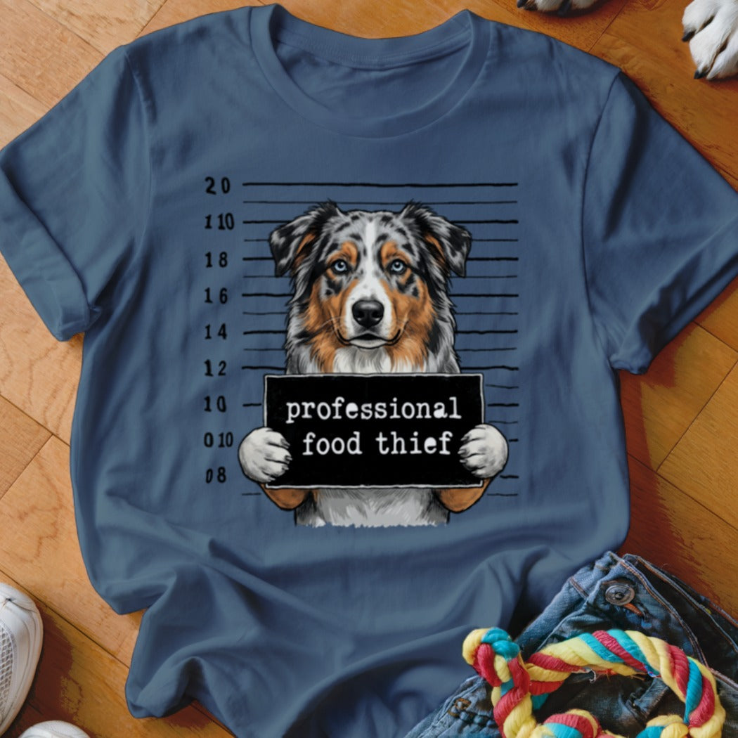 Australian Shepherd in mugshot holding "professional food thief" sign.