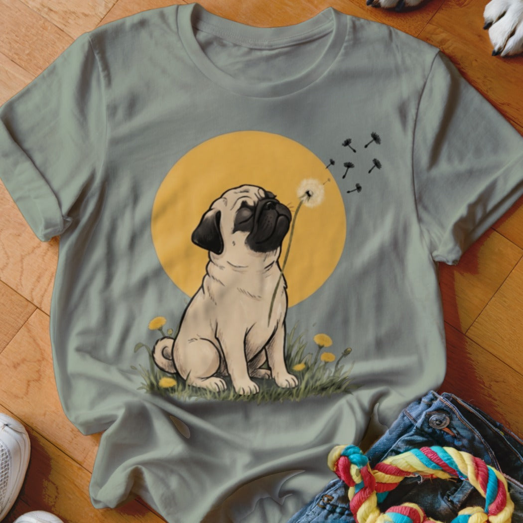 Sage green t-shirt featuring an illustrated pug blowing dandelion seeds against a yellow sun background.