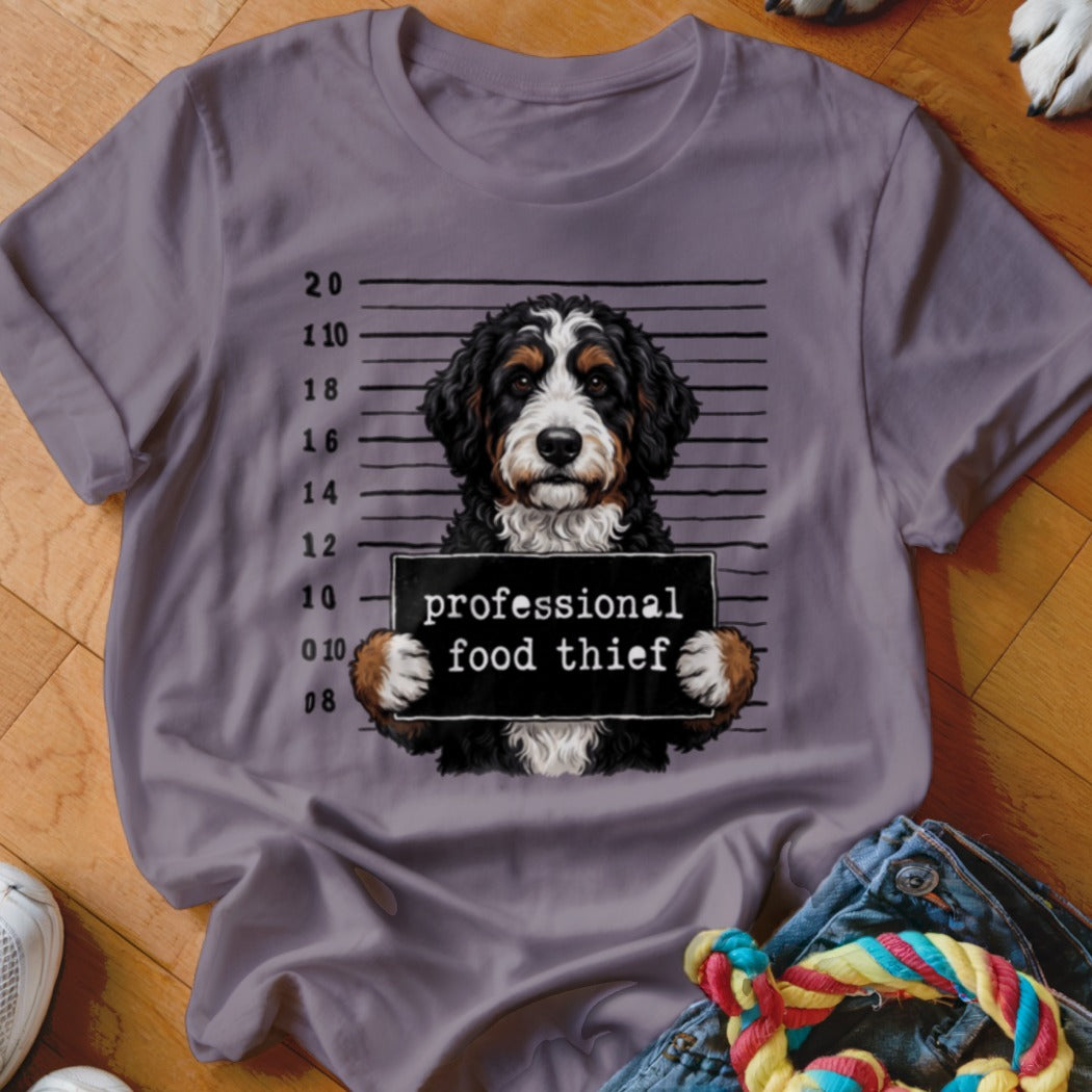 Bernese Mountain Dog in mugshot with "professional food thief" sign.