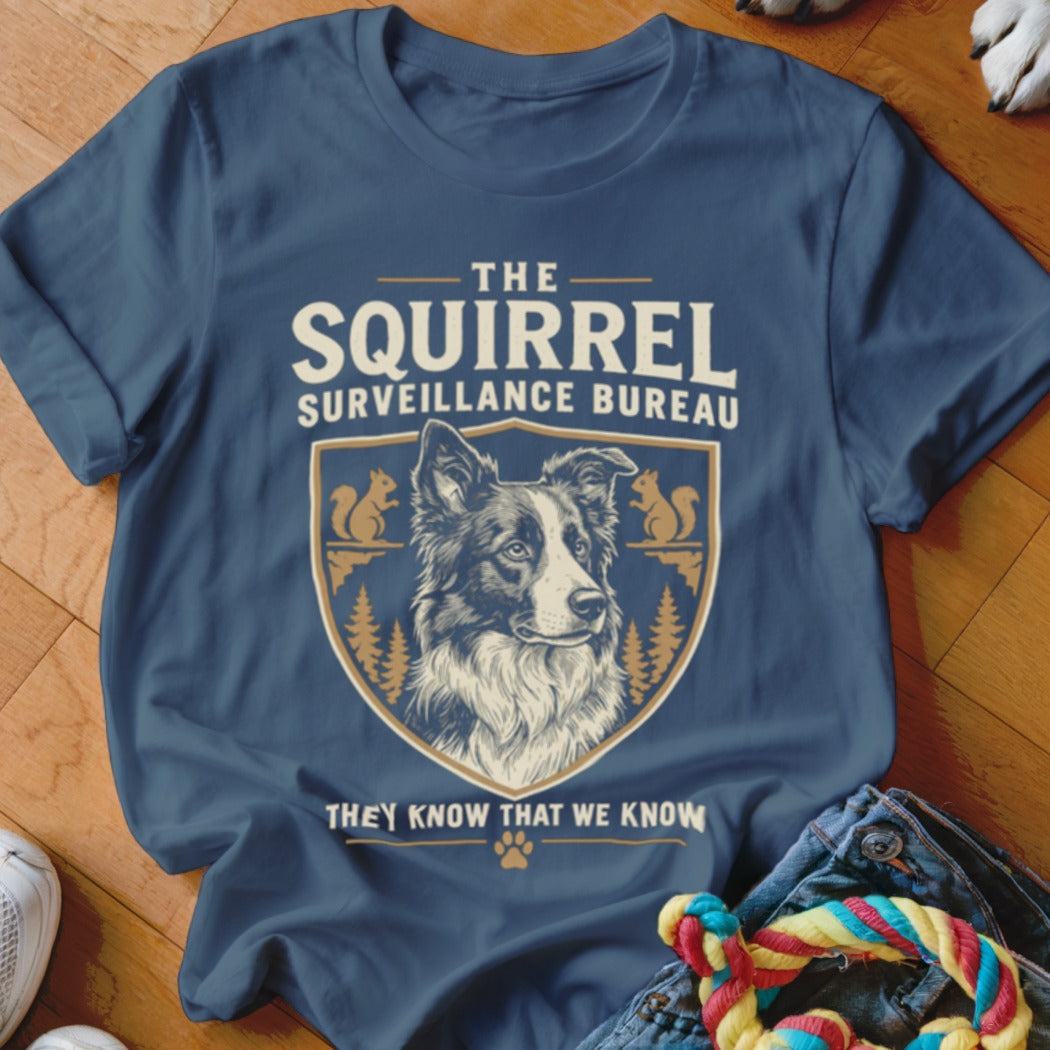 A dark blue t-shirt printed with a border collie illustration, squirrel graphics, and text reading The Squirrel Surveillance Bureau.