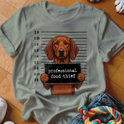 Dog mugshot with "professional food thief" sign on a light grey t-shirt.