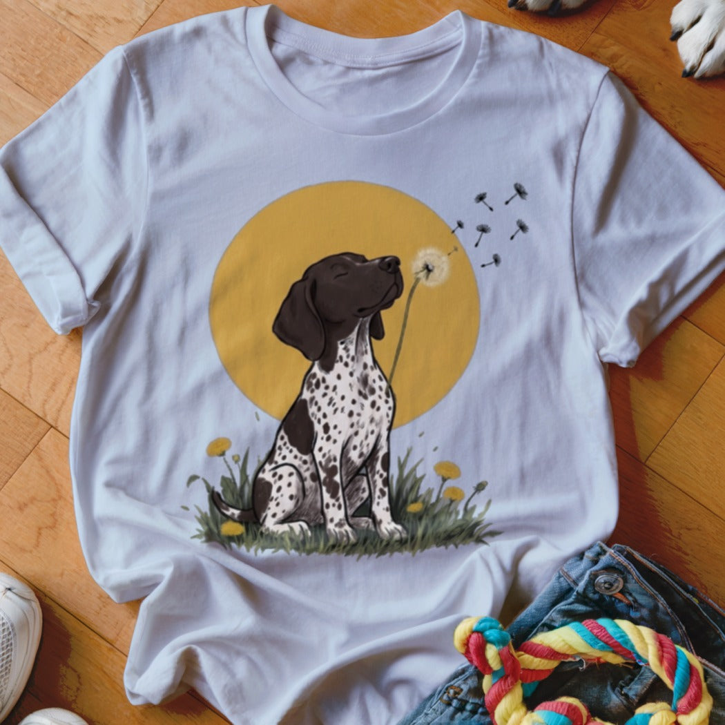 White t-shirt featuring an illustration of a spotted dog blowing dandelion seeds against a yellow circle background.