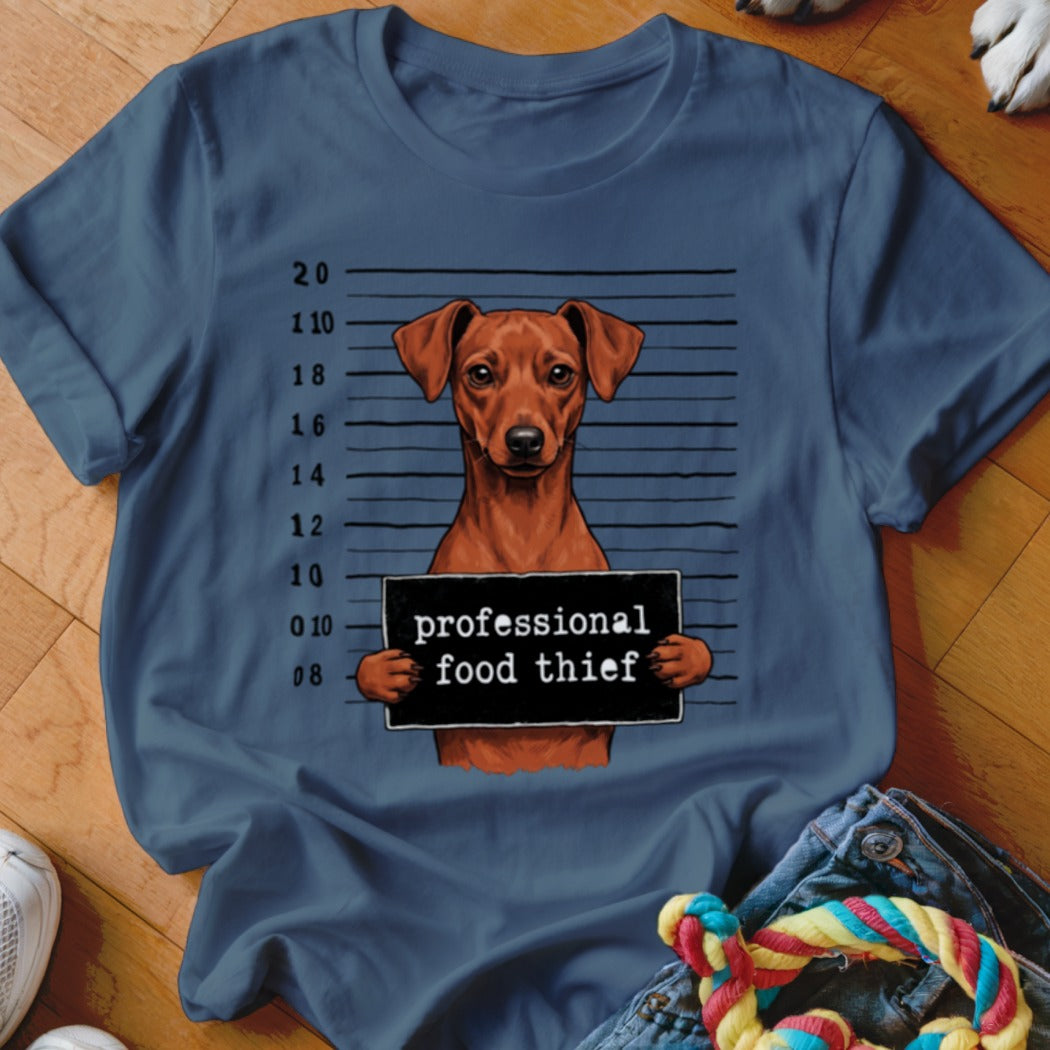 Brown dog mugshot with "professional food thief" sign on blue t-shirt.