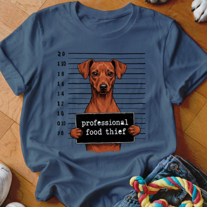 Brown dog mugshot with "professional food thief" sign on blue t-shirt.