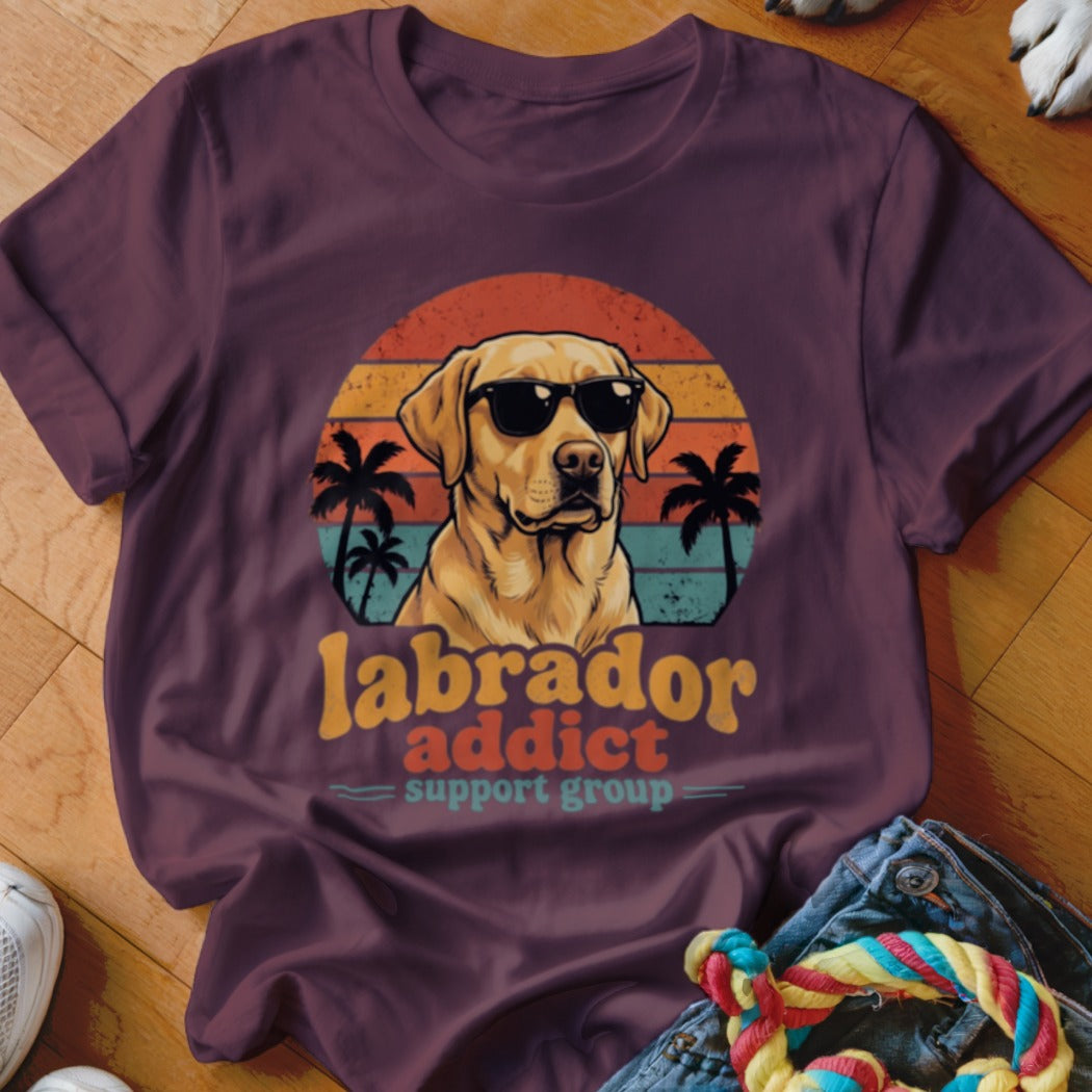 A maroon t-shirt with a vintage graphic of a yellow Labrador in sunglasses, palm trees, and the text Labrador Addict Support Group.