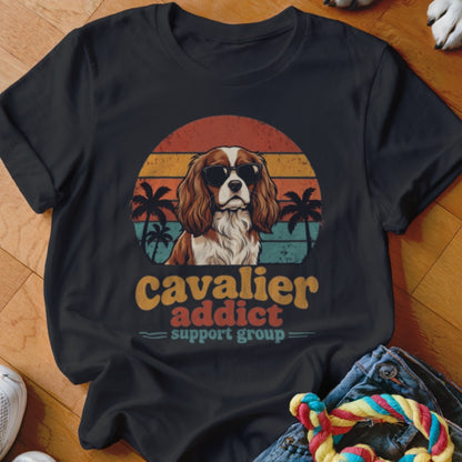 A black t-shirt features a graphic of a Cavalier King Charles Spaniel wearing sunglasses against a sunset.