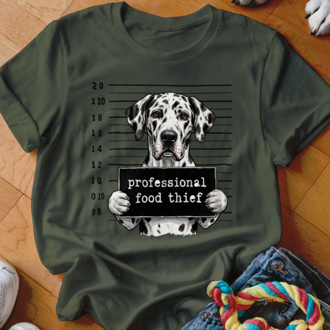 Dalmatian dog in mugshot with "professional food thief" sign on olive green t-shirt.