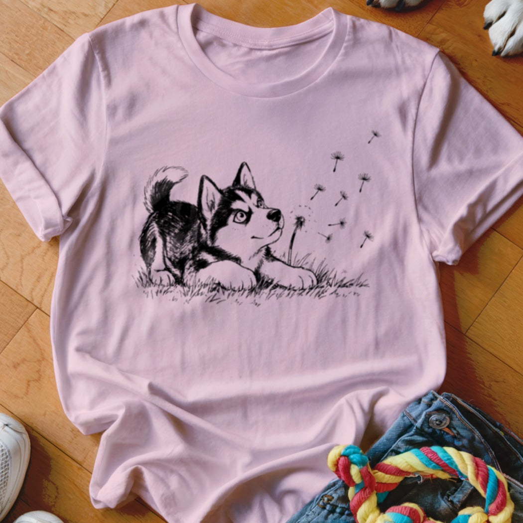 A pink crewneck t-shirt featuring a black and white sketch of a husky puppy looking at blowing dandelions.