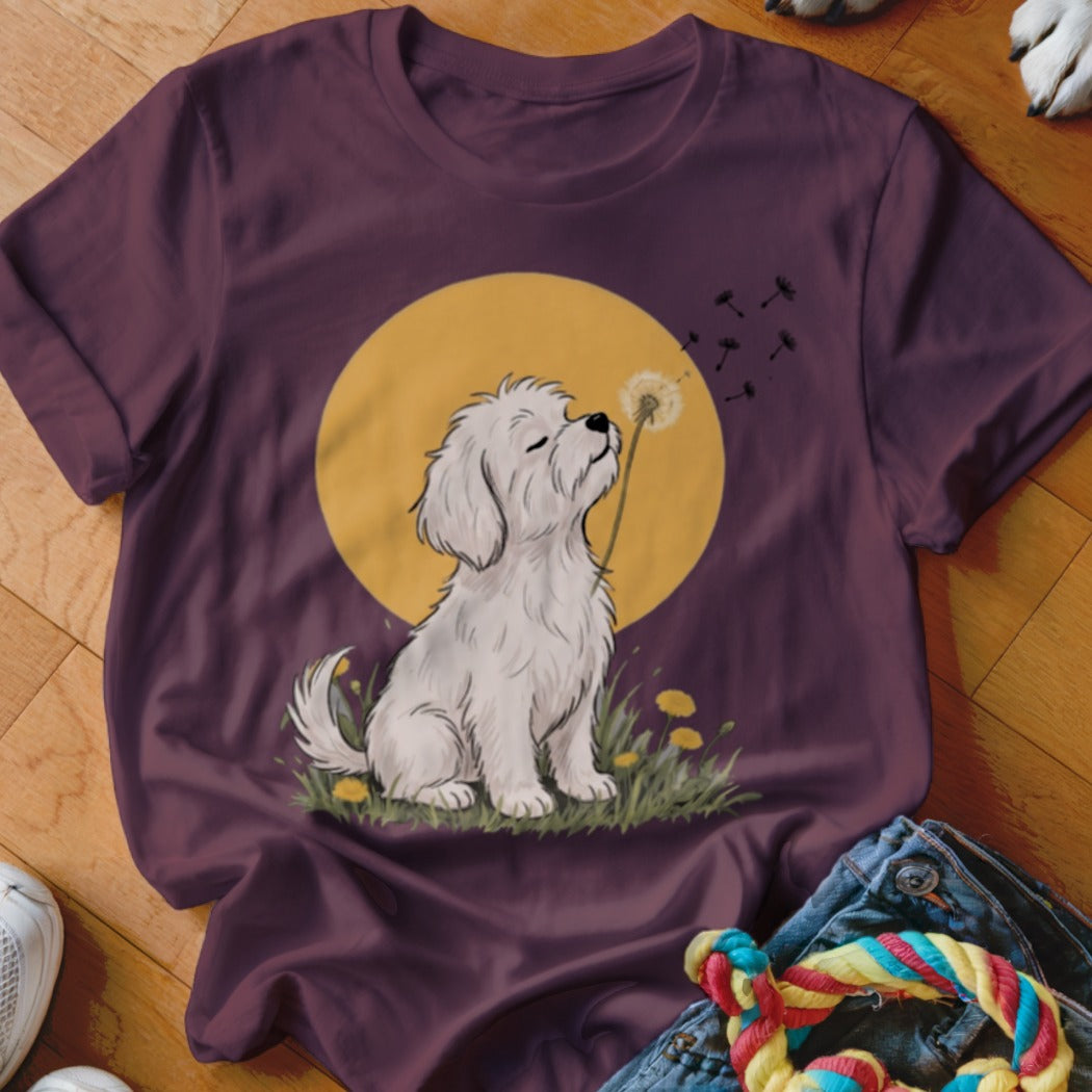 Plum-colored t-shirt featuring a cartoon illustration of a fluffy white dog blowing dandelion seeds against a yellow moon.