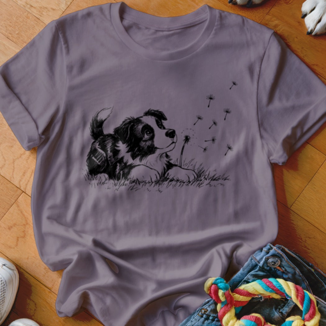 A mauve t-shirt features a black graphic of a puppy watching floating dandelion seeds.