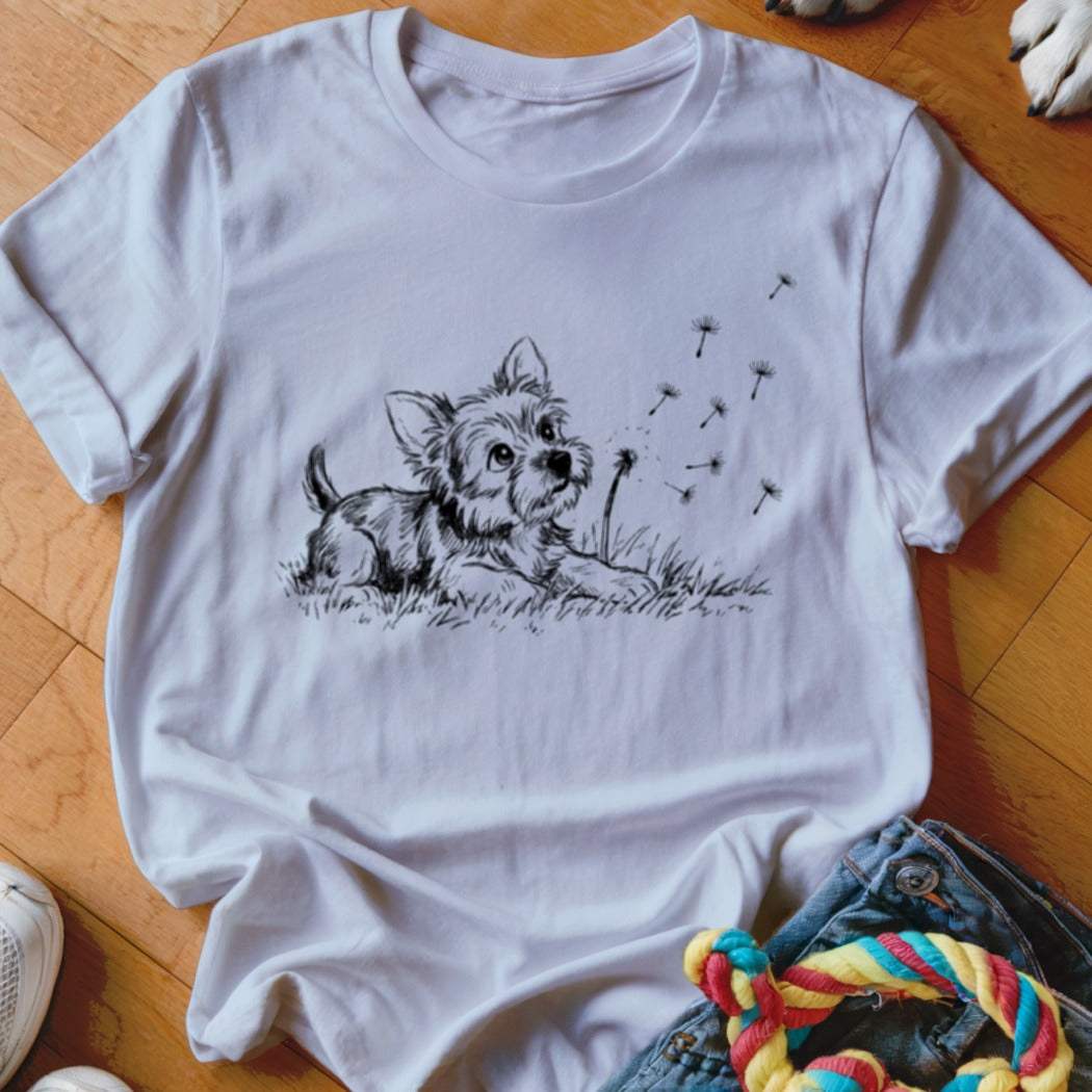 A white crewneck t-shirt features a black line drawing of a puppy watching floating dandelion seeds.