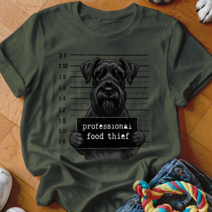Black schnauzer mugshot with "professional food thief" sign on olive shirt.