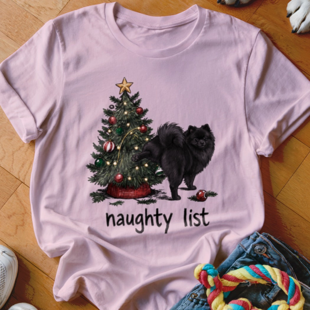 Black Pomeranian dog near Christmas tree with "naughty list" text on pink t-shirt.