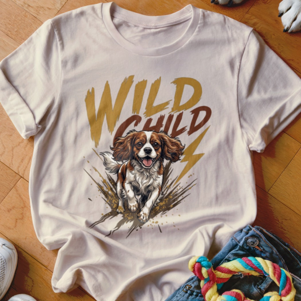 A light-colored t-shirt featuring a graphic of a running King Charles Spaniel and the text WILD CHILD.