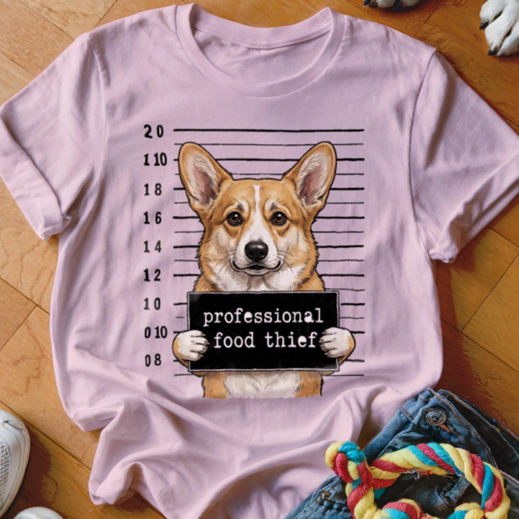 Corgi mugshot with "professional food thief" sign on pink t-shirt.
