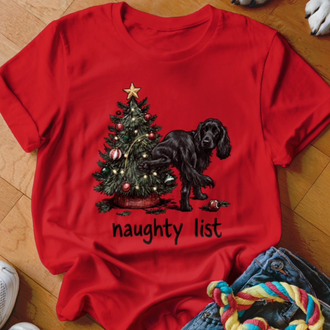 Black dog next to Christmas tree with text "naughty list" on red shirt.