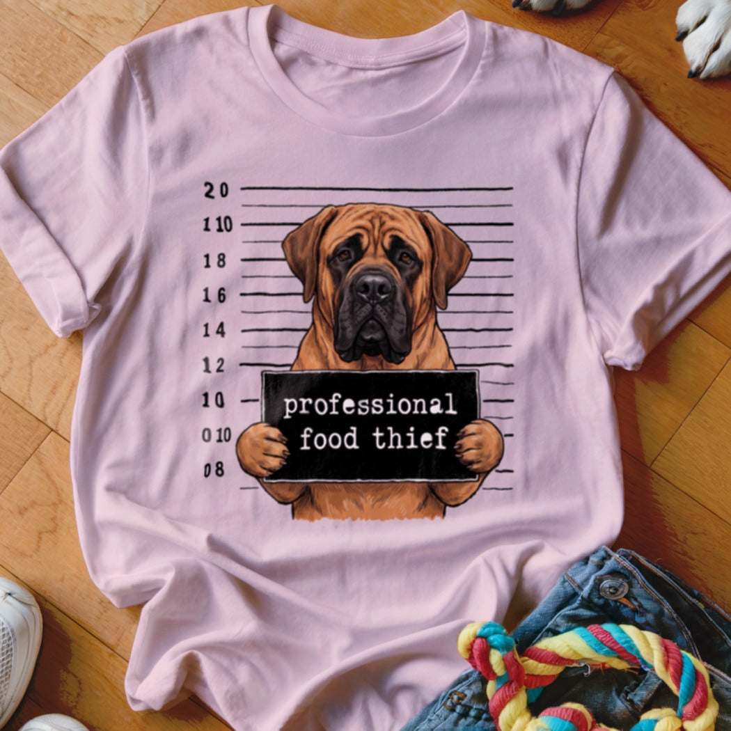 Bullmastiff mugshot with sign "professional food thief" on pink t-shirt.