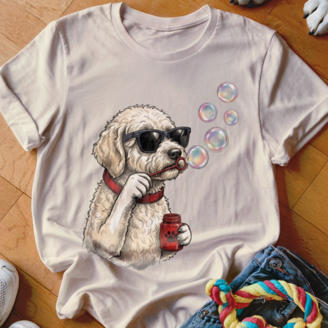 A cream-colored t-shirt featuring a graphic of a fluffy dog wearing sunglasses and blowing bubbles.