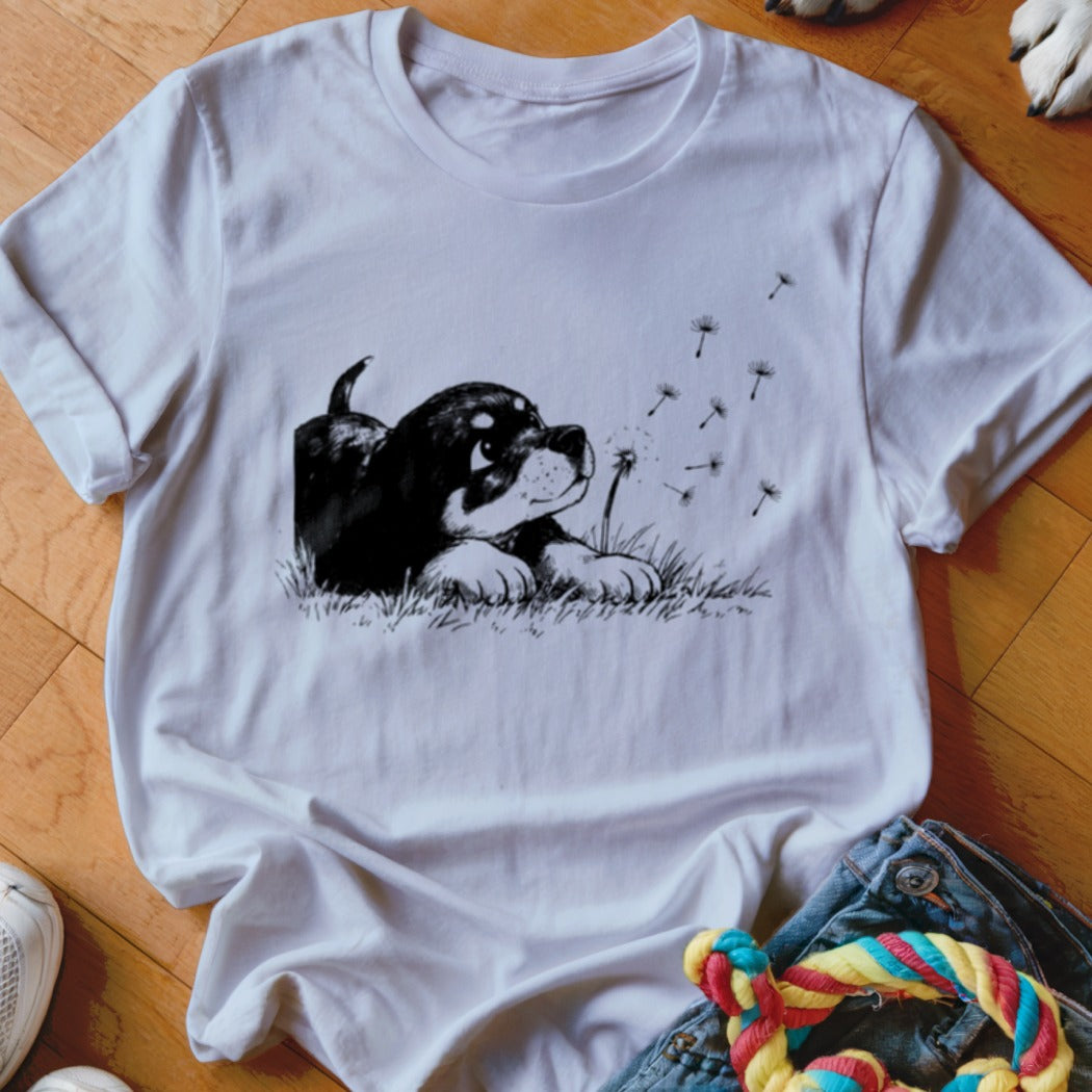 A white short-sleeved t-shirt featuring a black and white illustration of a puppy blowing dandelion seeds.