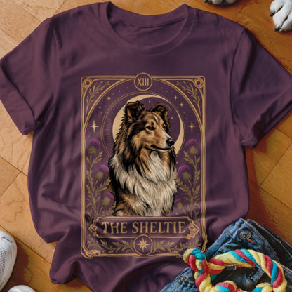 A dark purple crewneck t-shirt featuring a tarot card style Sheltie dog graphic centered on the chest.