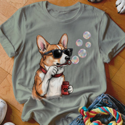 A sage green t-shirt featuring a graphic of a corgi wearing sunglasses and blowing soap bubbles.