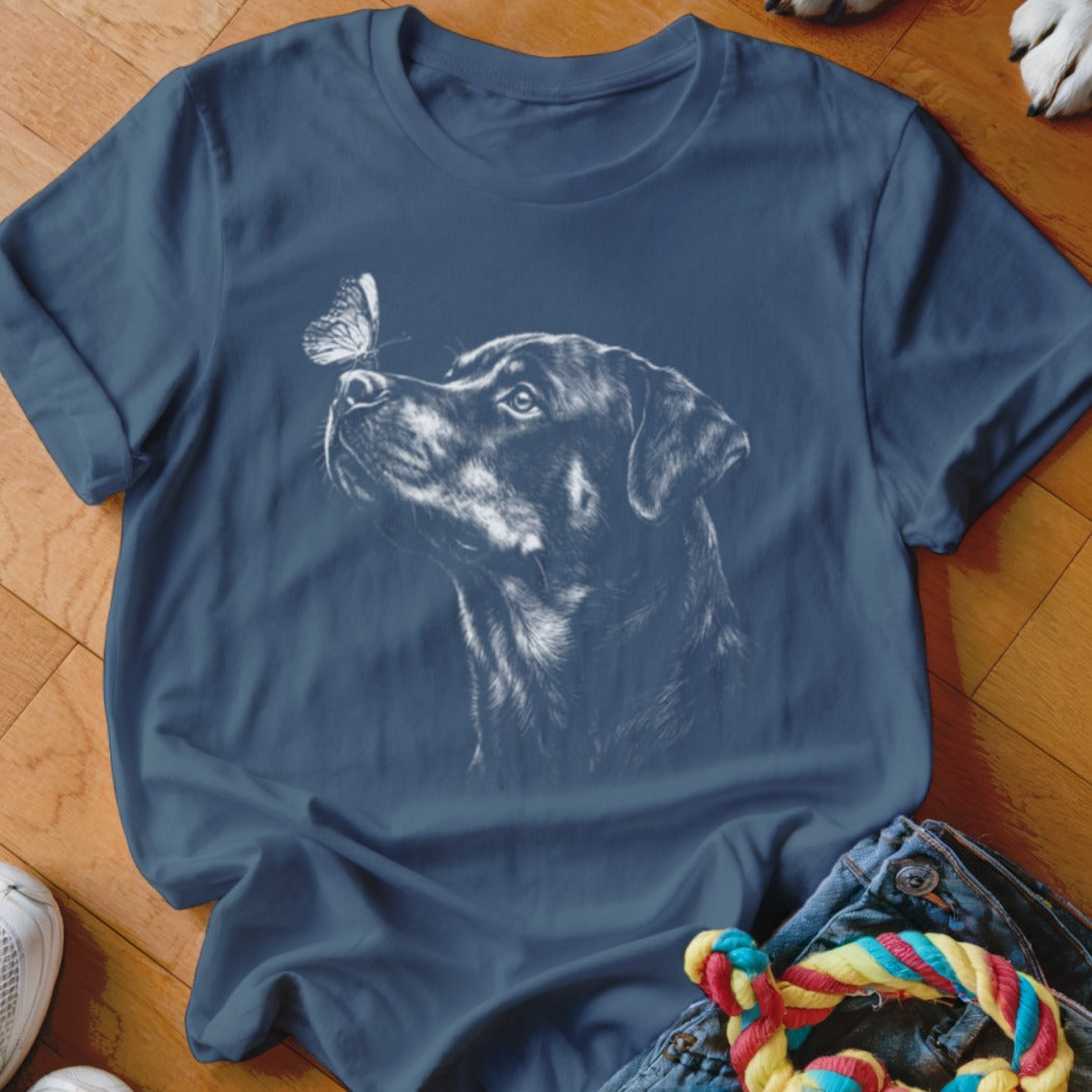 A dark blue t-shirt with a white graphic print of a Rottweiler looking at a butterfly on its nose.