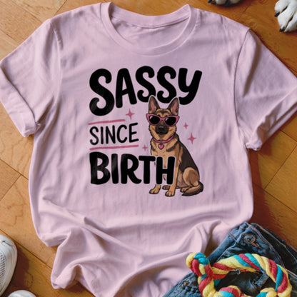 German Shepherd wearing sunglasses with text "Sassy Since Birth" on a pink t-shirt.