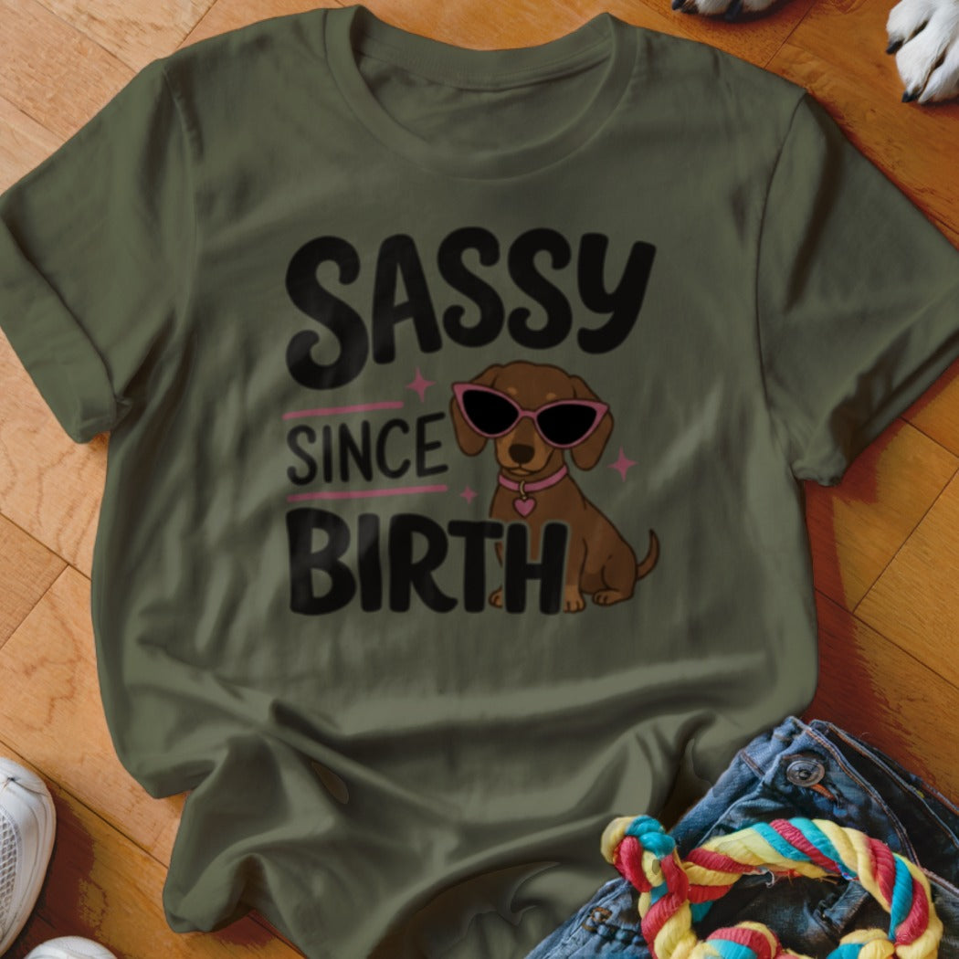 Olive green t-shirt with cartoon dachshund wearing sunglasses and "SASSY SINCE BIRTH" text.