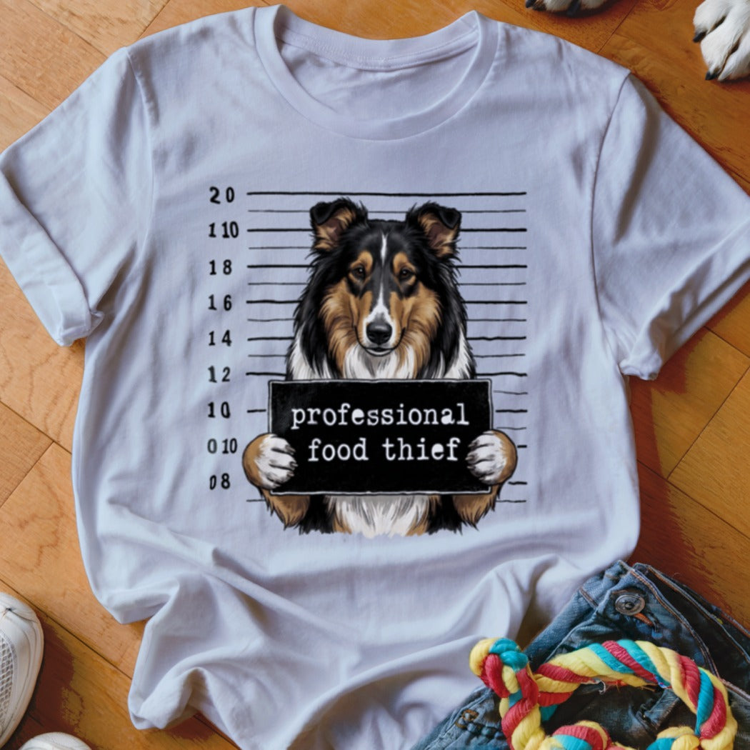 Collie dog mugshot with "professional food thief" sign on t-shirt.