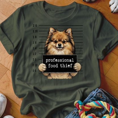Pomeranian dog holding "professional food thief" sign in mugshot style.
