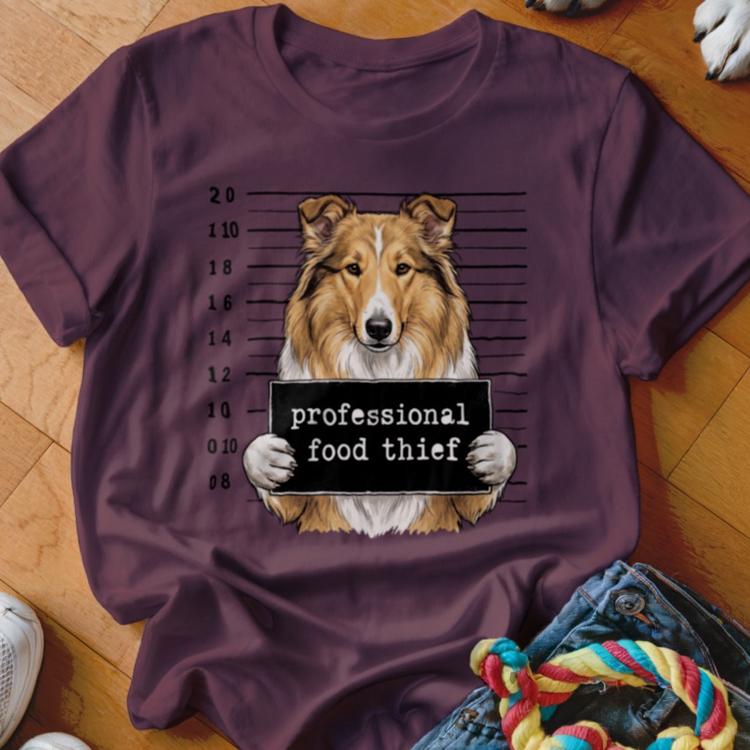 Collie dog mugshot with "professional food thief" sign on a t-shirt.