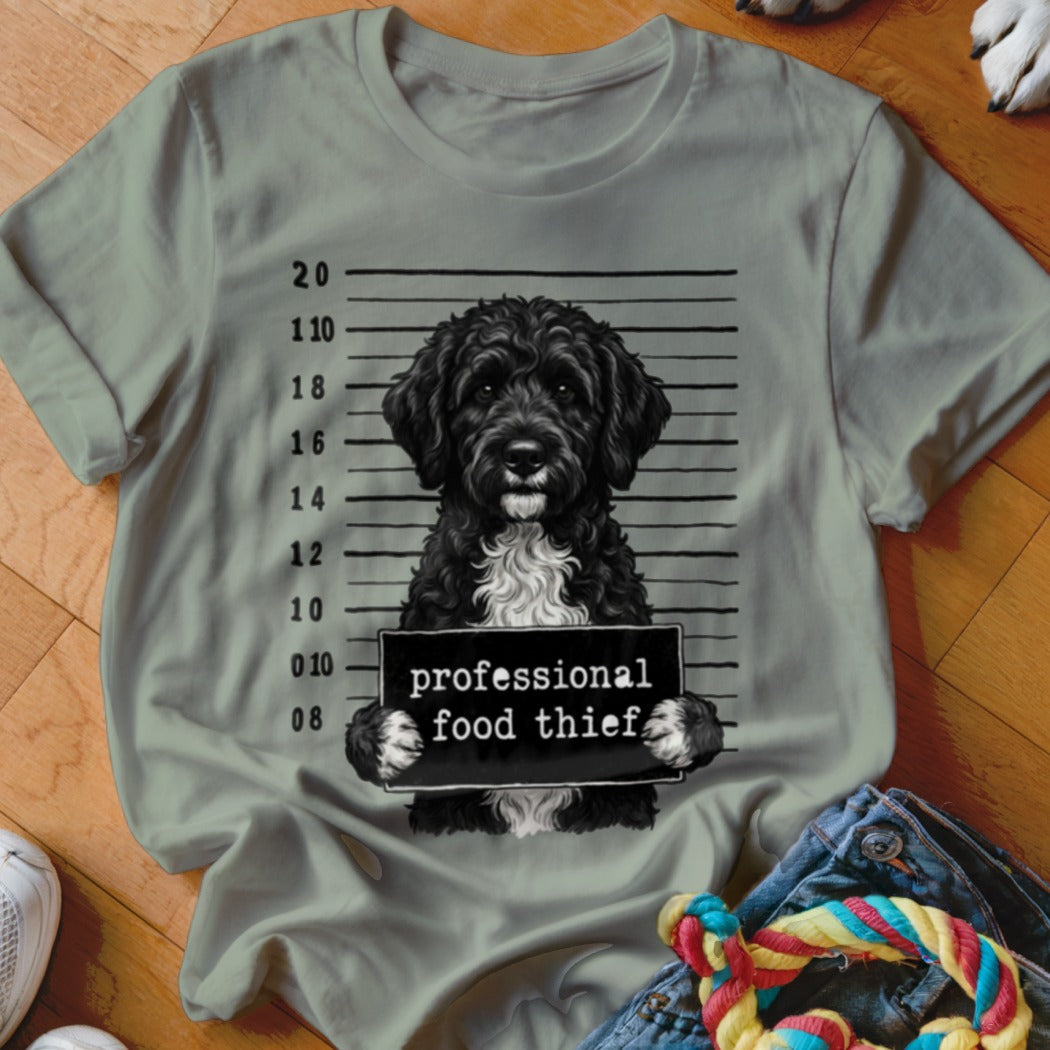 Black dog with white chest, holding sign "professional food thief" in mugshot.