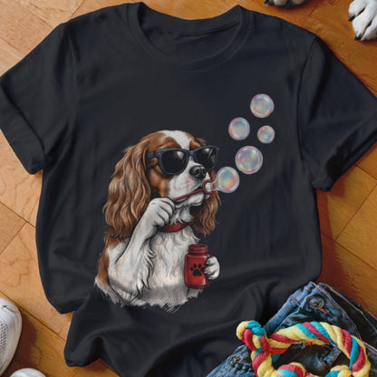 A black t-shirt printed with a Cavalier King Charles Spaniel wearing sunglasses and blowing bubbles.