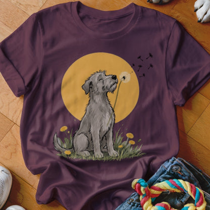 A plum-colored t-shirt features a graphic of a grey dog sitting in grass before a yellow moon, blowing dandelion seeds.