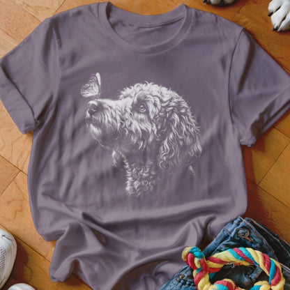 A purple t-shirt featuring a white sketched graphic of a curly-haired dog looking at a butterfly on its nose.