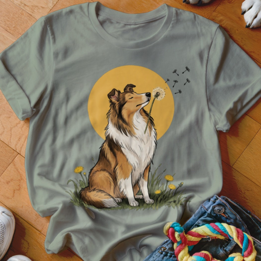 Sage green t-shirt featuring an illustration of a collie blowing a dandelion against a yellow sun.