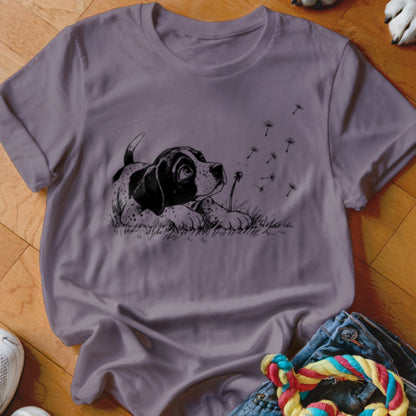 A purple short-sleeved t-shirt featuring a black-and-white graphic of a puppy watching dandelion seeds blow away.