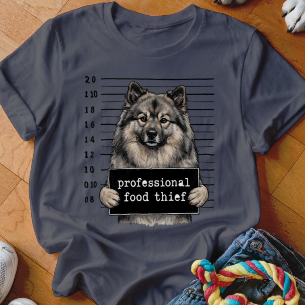 Keeshond in mugshot pose holding "professional food thief" sign.