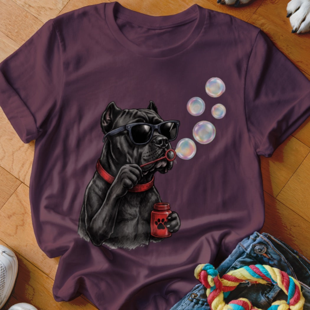 A plum-colored t-shirt displays an illustration of a black dog wearing sunglasses, blowing bubbles.