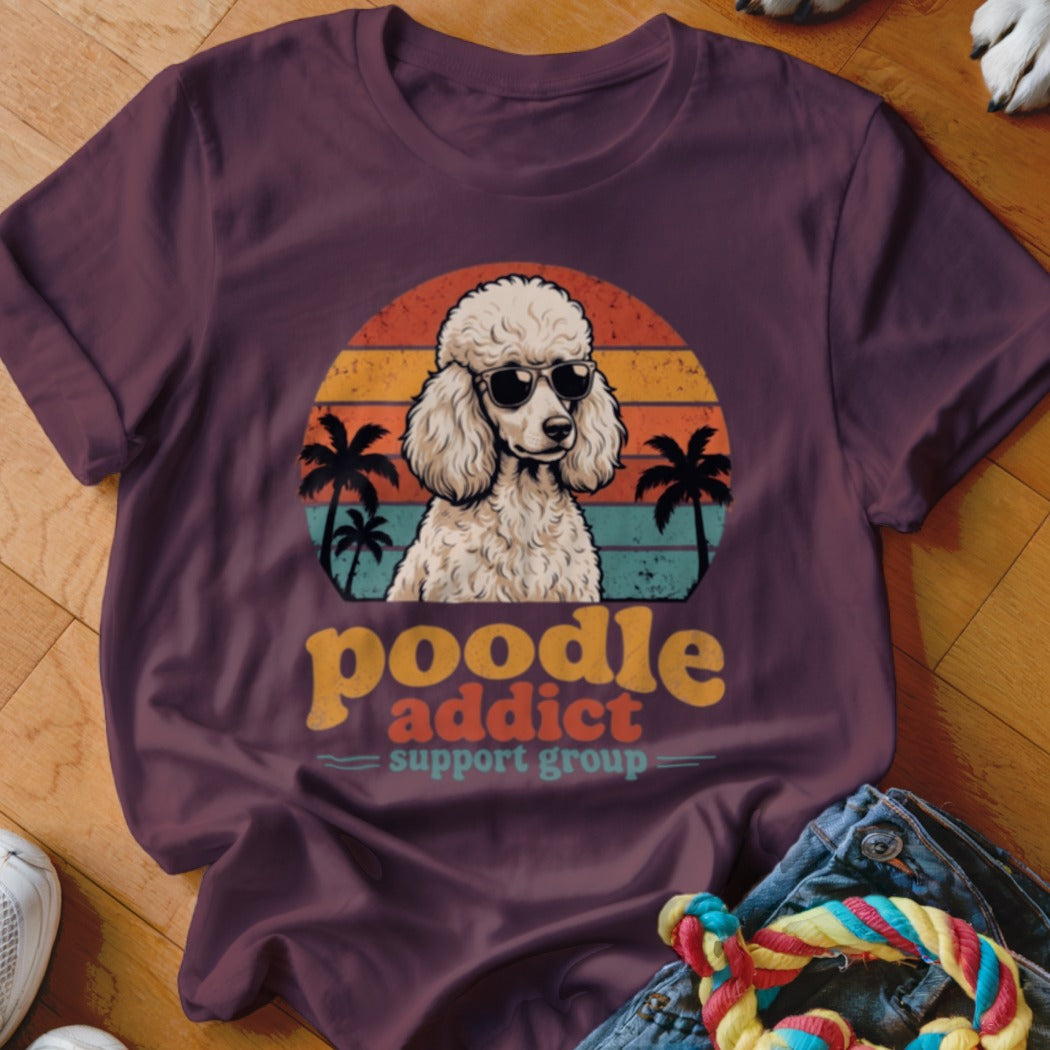A maroon t-shirt featuring a retro graphic of a poodle wearing sunglasses against a sunset.