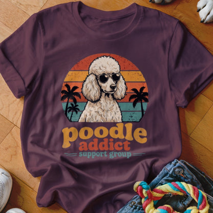 A maroon t-shirt featuring a retro graphic of a poodle wearing sunglasses against a sunset.