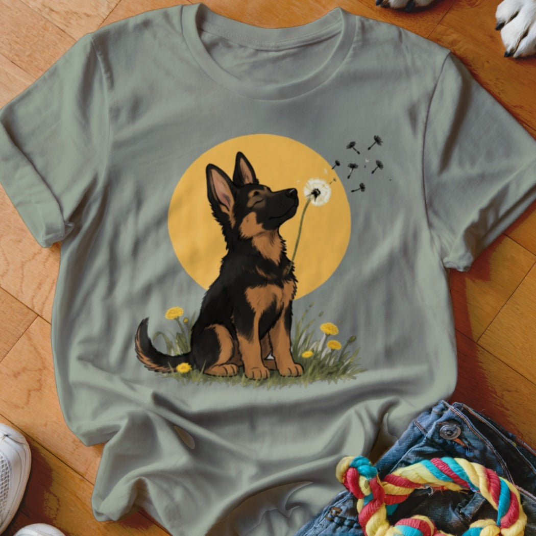 Sage green t-shirt featuring a cartoon German Shepherd puppy blowing dandelion seeds against a yellow sun.