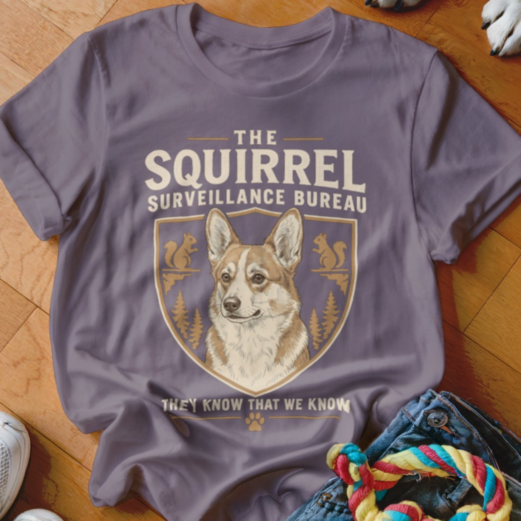 A purple t-shirt featuring a corgi graphic and the text The Squirrel Surveillance Bureau.