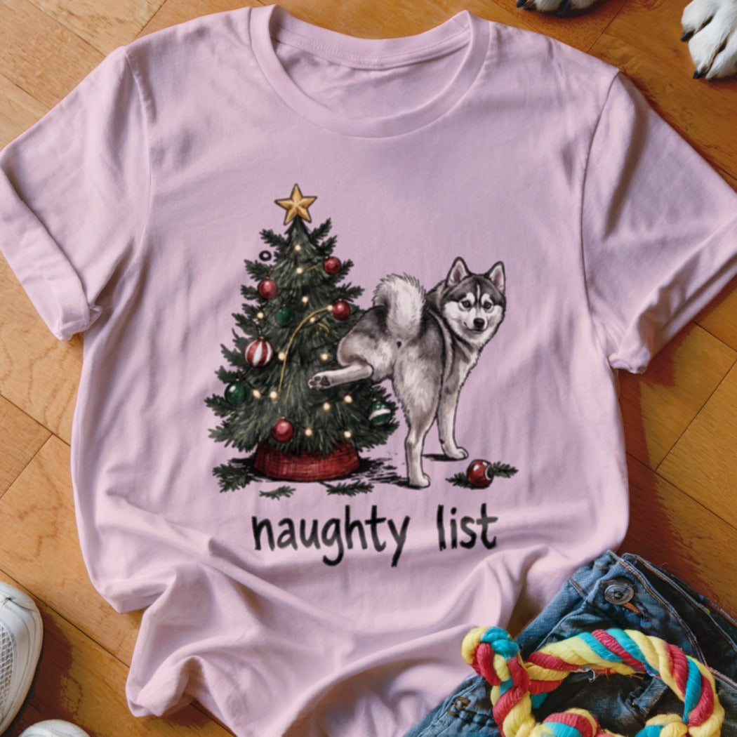 Husky dog by Christmas tree with text "naughty list" on pink shirt.