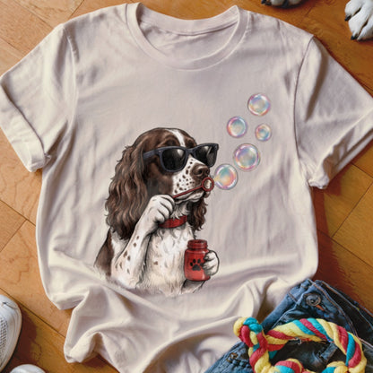 Light-colored t-shirt featuring a graphic of a brown and white spaniel wearing sunglasses and blowing bubbles.