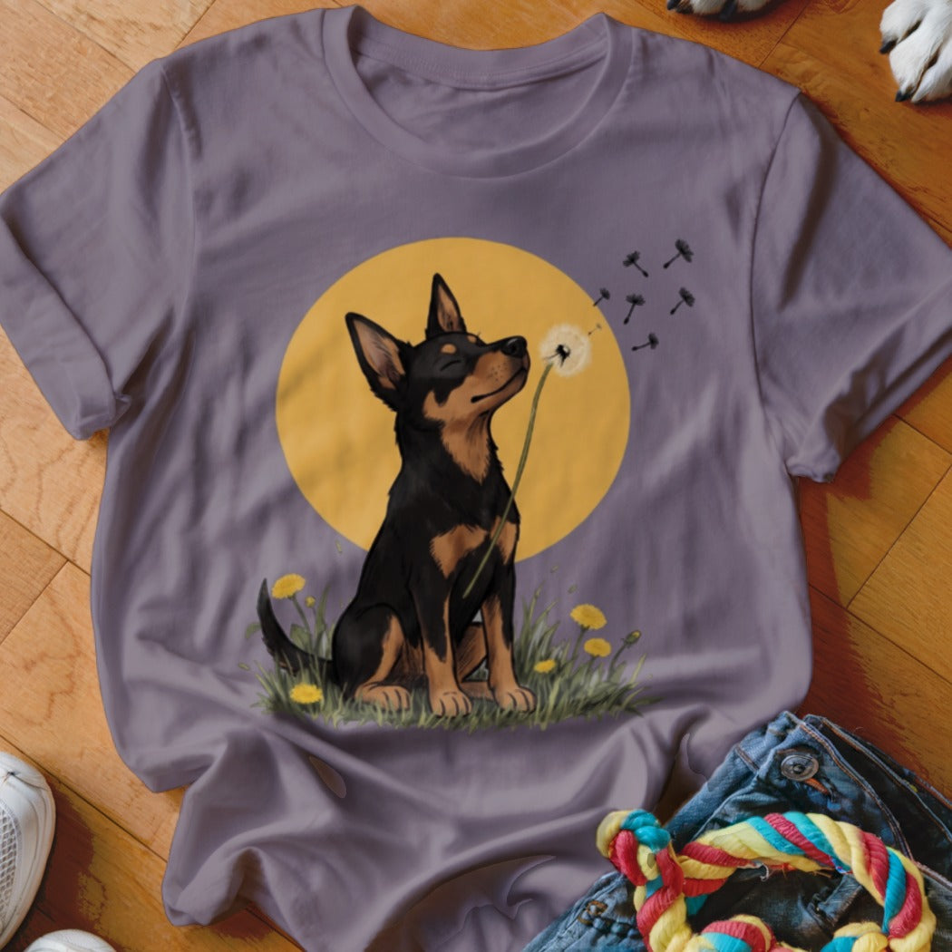 A purple t-shirt featuring an illustration of a black and tan dog sitting before a yellow sun and sniffing a dandelion.