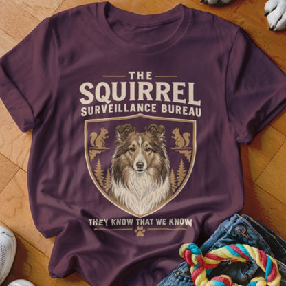A dark purple t-shirt featuring a Sheltie graphic with text reading The Squirrel Surveillance Bureau.